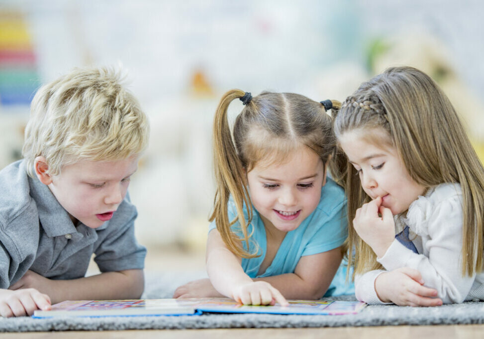 Three young children gathered around a book and reading
