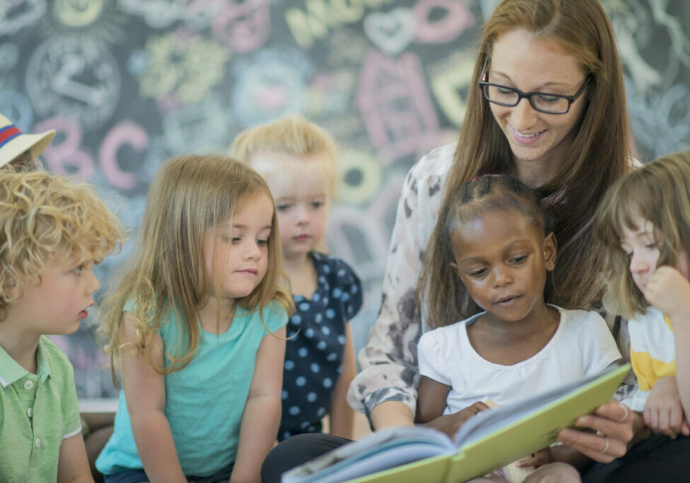 A teacher reading to a group of preschoolers as they help